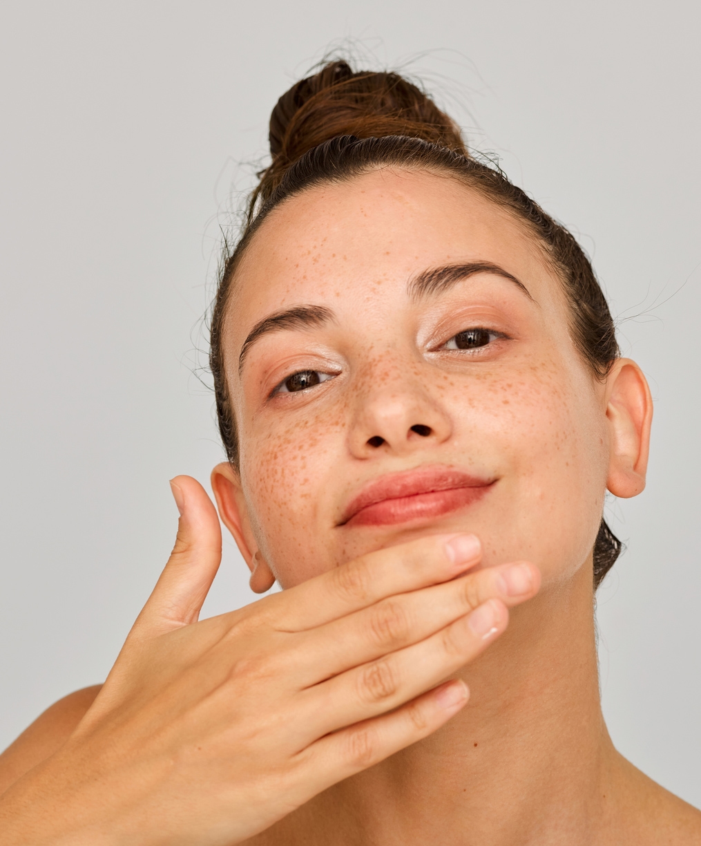 Woman with freckles, beaming at camera, touching her chin with her hand