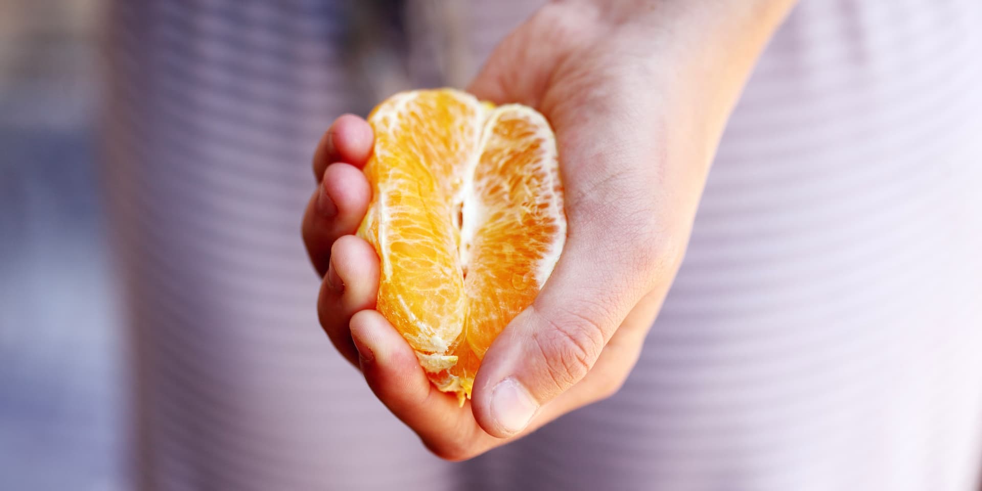 La mano de una mujer blanca, sosteniendo media naranja