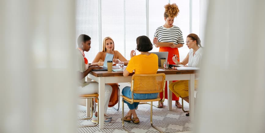 Group of female colleagues in casual clothes sitting at table with laptop and discussing details of project while working together in a co-working space