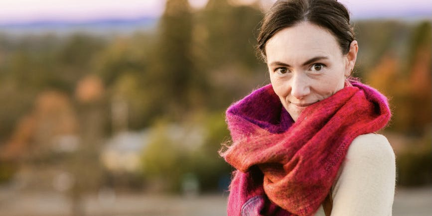 Portrait of beautiful young white woman looking at the camera wearing fa uschia wool scarf, taking a walk by the countryside in cold fall weather.