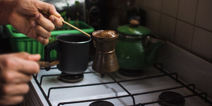 Closeup photo of a Latin American man preparing Turkish coffee on the gas stove in the kitchen.