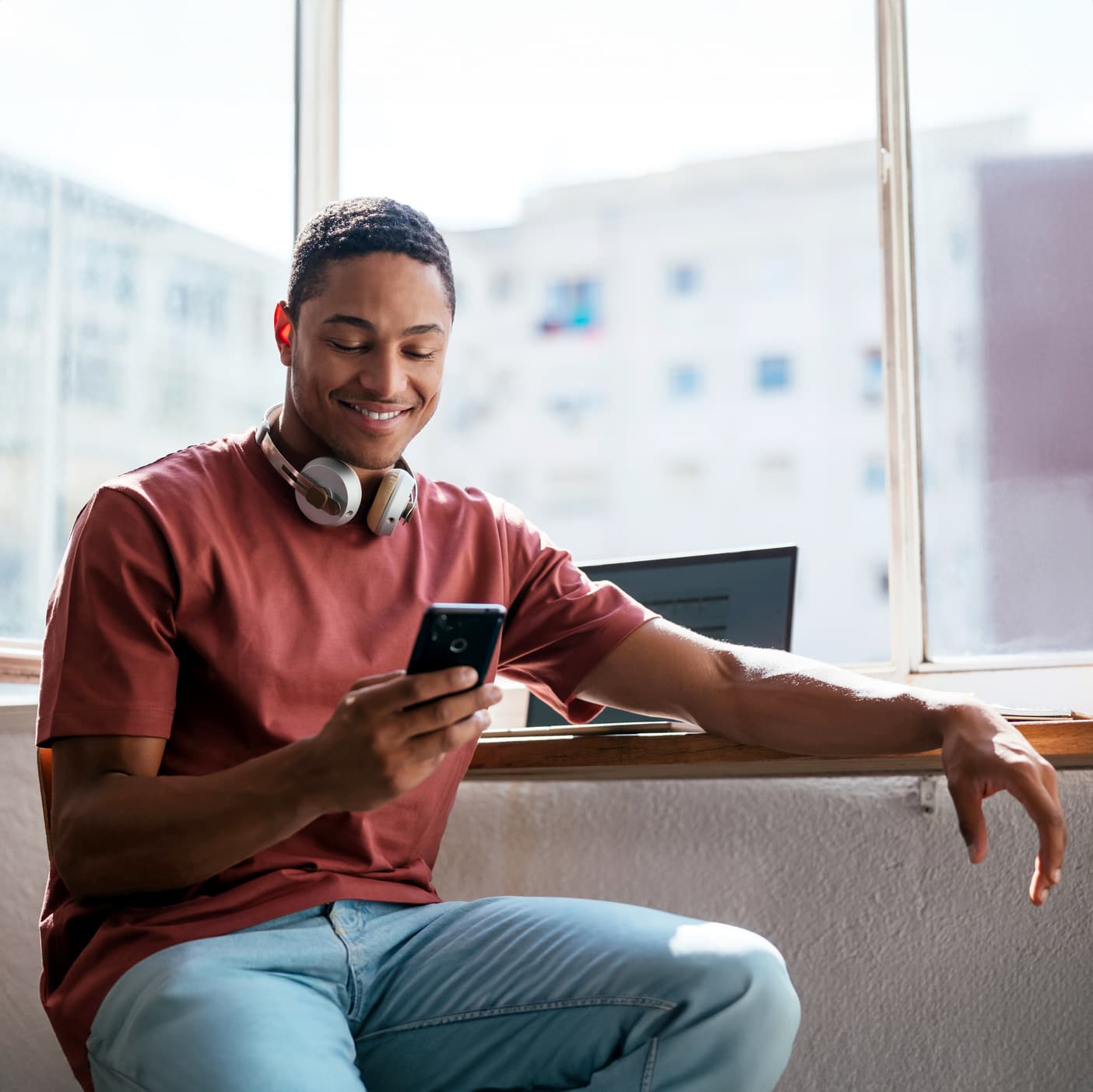 Black man looking at his phone while at a desk by a window, smiling