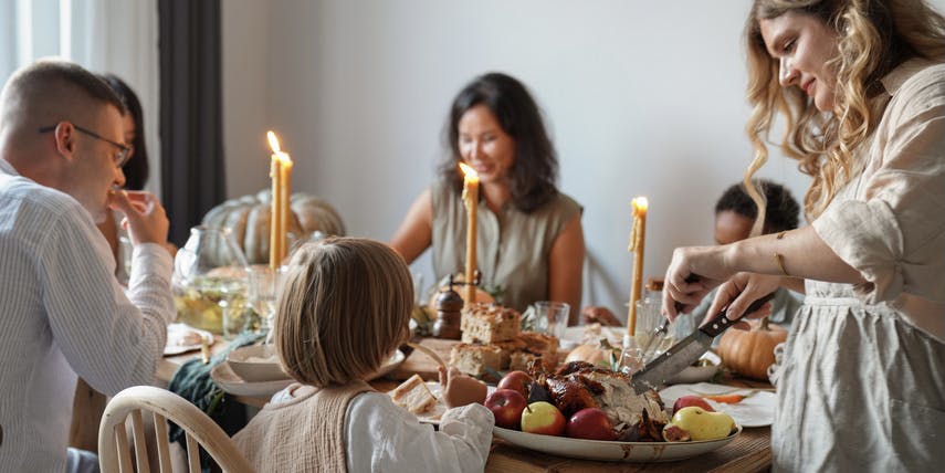 Family and friends with children gather at a festive Thanksgiving table decorated with candles and Autumn foods and have fun