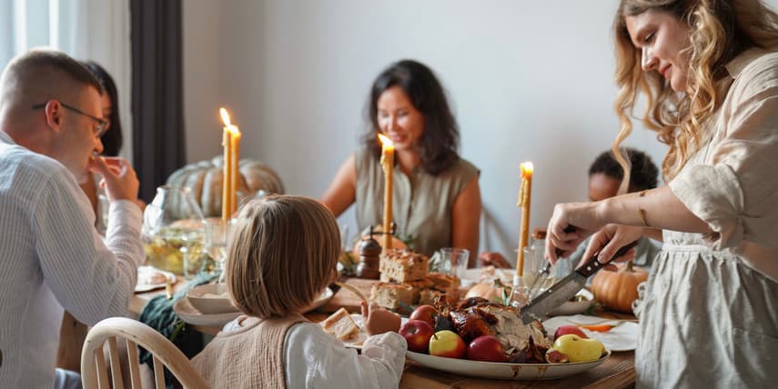 Family and friends with children gather at a festive Thanksgiving table decorated with candles and Autumn foods and have fun