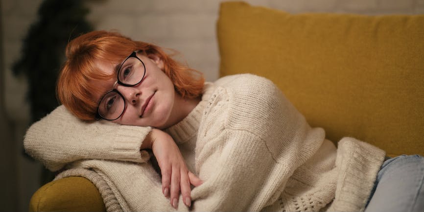 A young white woman with red hair rests on a couch during the holidays