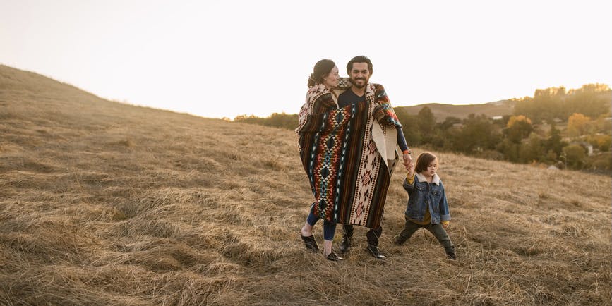 Familia con un niño pequeño cubriéndose con una manta geométrica ecuatoriana dando un paseo por el campo al atardecer, pasando tiempo de calidad juntos en otoño