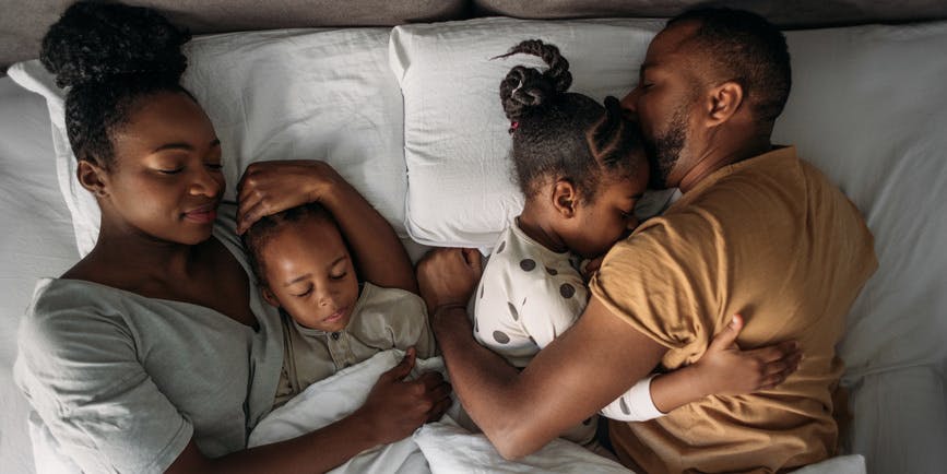 Fotografía desde arriba de una familia negra en la cama, con un hombre y una mujer abrazando a dos niños pequeños.
