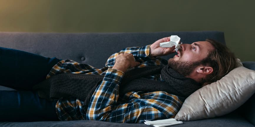 Young ill man with cold and high fever lying on sofa at home. Cold and flu season.