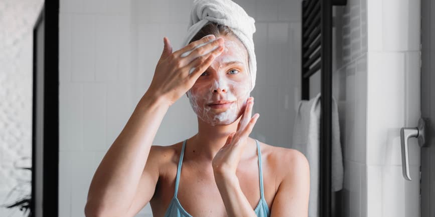 Pretty woman in her twenties washing face with soap in bathroom.