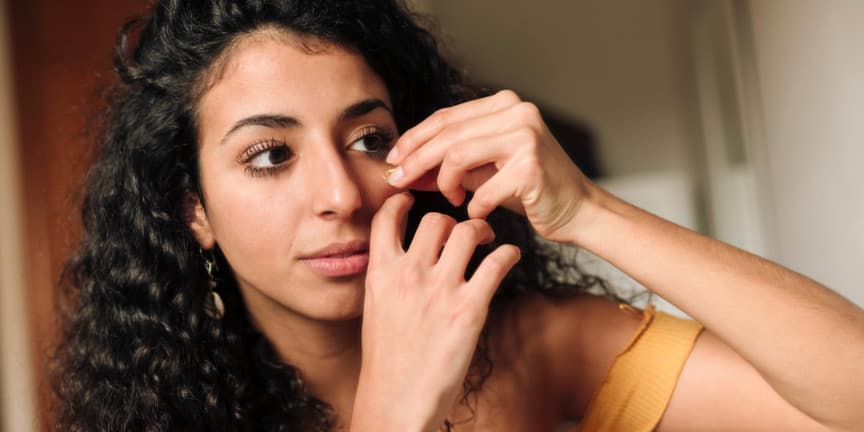 Young woman with olive skin, applying essential oil to hydrate her face as part of her beauty routine.