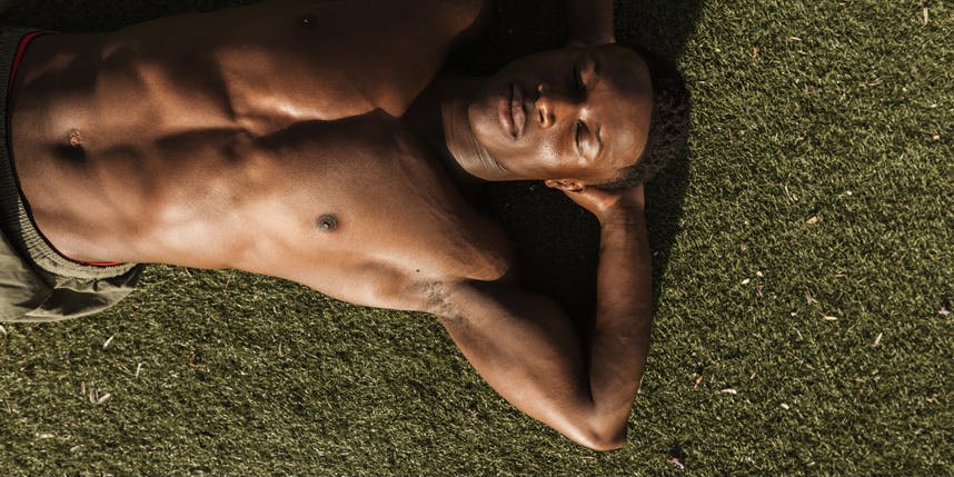 A young Brazilian man with an athletic appearance rests in the bright sun on the grass after an outdoor sports session.