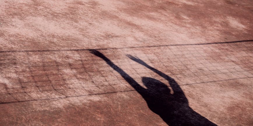 The shadow of a woman splays out on a tennis court, look like she's reaching over the net.