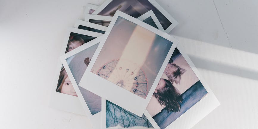 A dreamy toned photo of a stack of Polaroid photos with one showing a Ferris wheel on top.