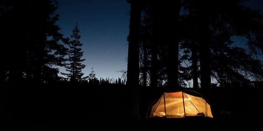 A glowing orange tent in the forest at night.