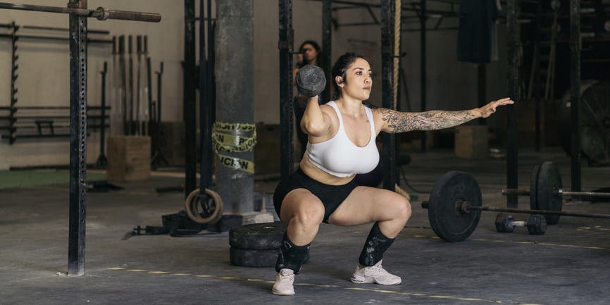 Strong young woman performs a barbell squat in a gym, she looks confident and focused.