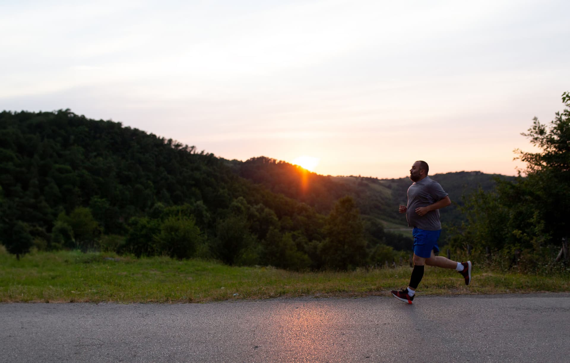 Man jogging on a bare road with a hillside and sunset in the background