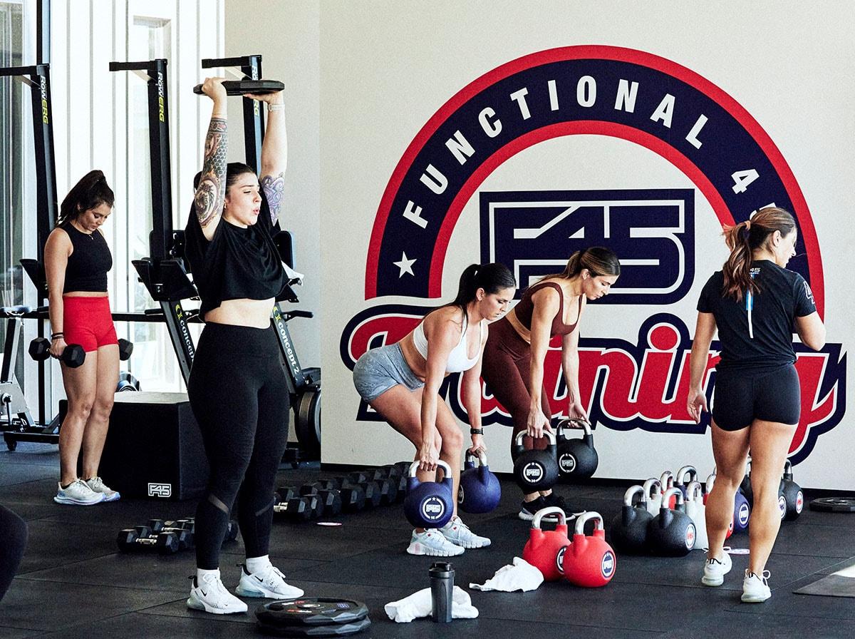 A F45 Training class where a trainer is assisting people lifting weights