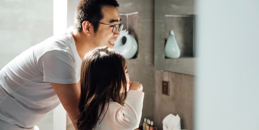 Young Asian father and cute little daughter brushing teeth together at home.