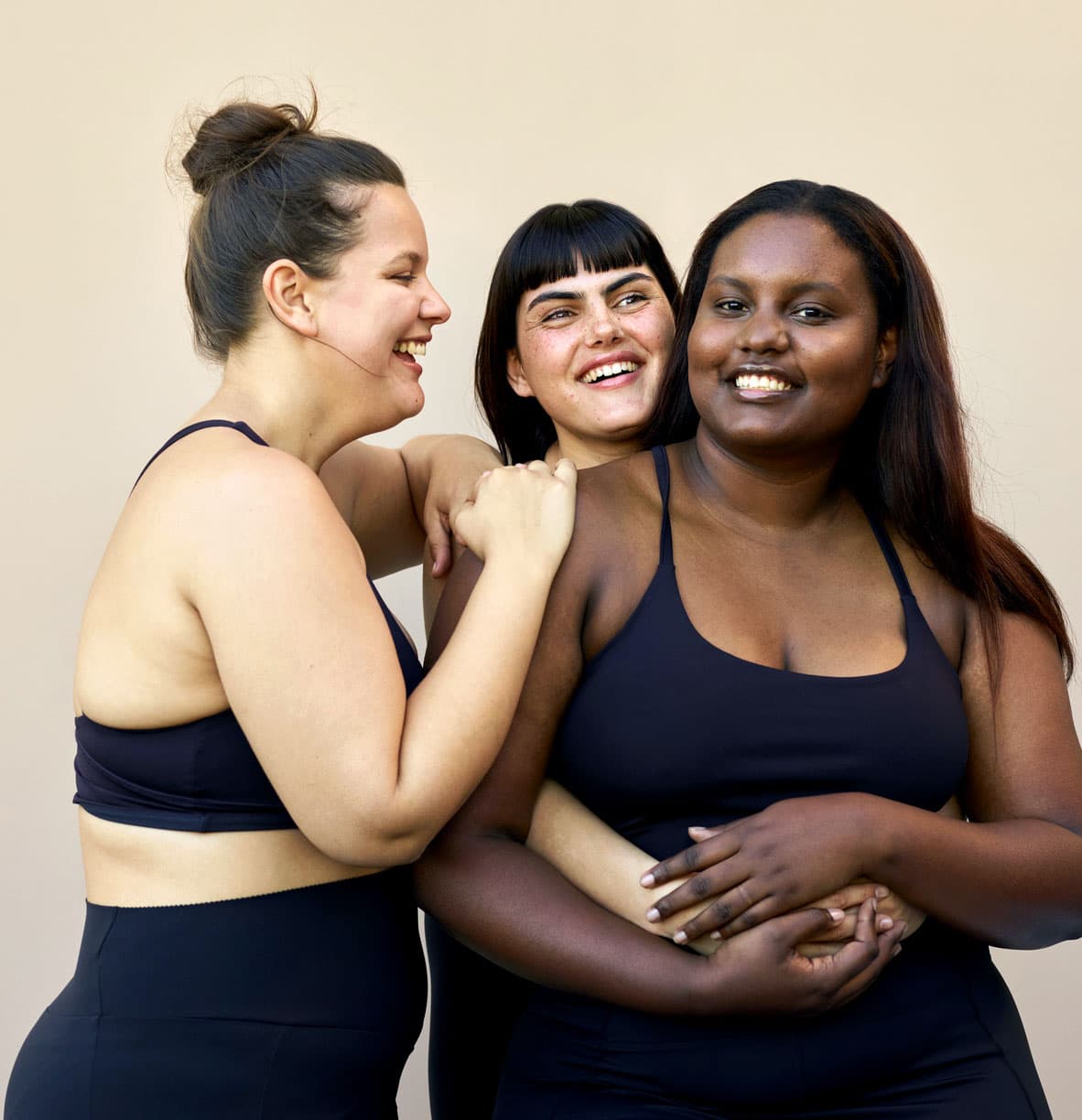 Three women wearing matching black workout clothes, hugging each other