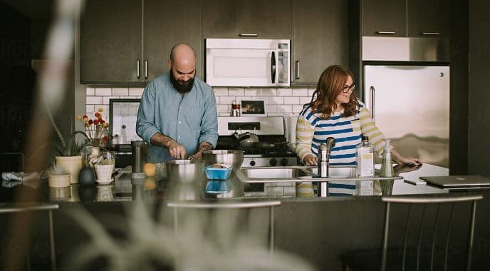 A couple prepares food in a modern kitchen with stainless steel appliances and natural light.