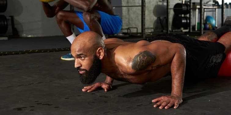 Two fit Black men doing weight ball exercises in a gym.