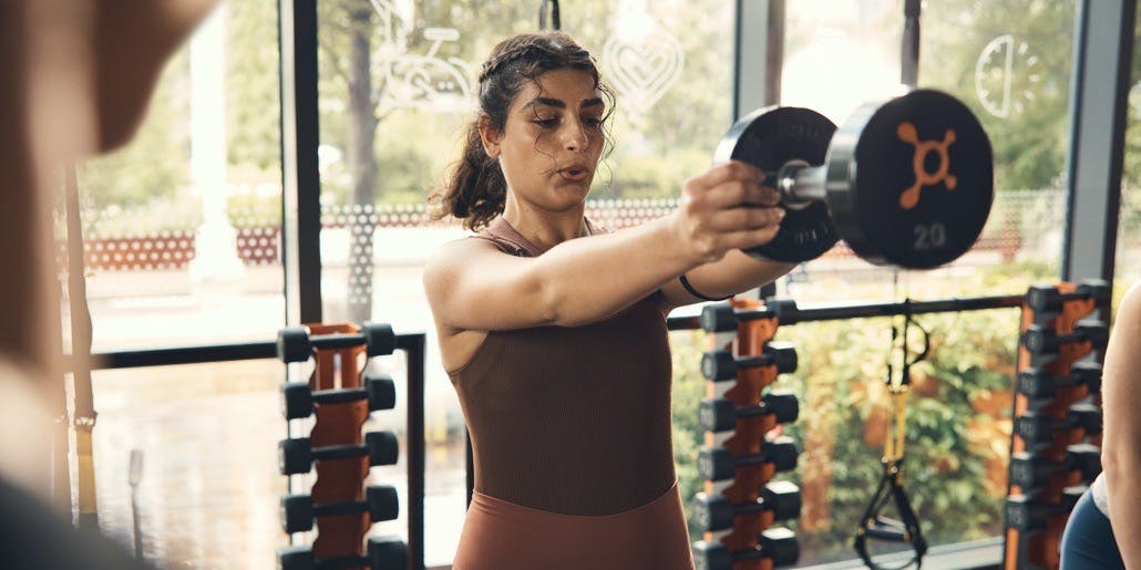 A young woman concentrates as she lifts a heavy weight during an Orangtheory Fitness class.