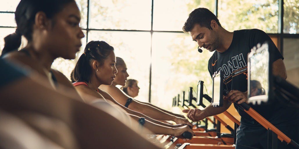 An Orangetheory Coach encourages a young woman on a rowing machine during an Orangetheory Fitness class.