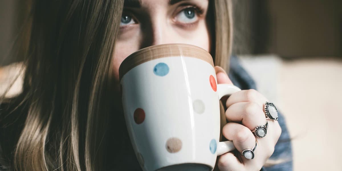 Closeup of a white woman with long, dark blond hair sipping out of a polka-dot mug.