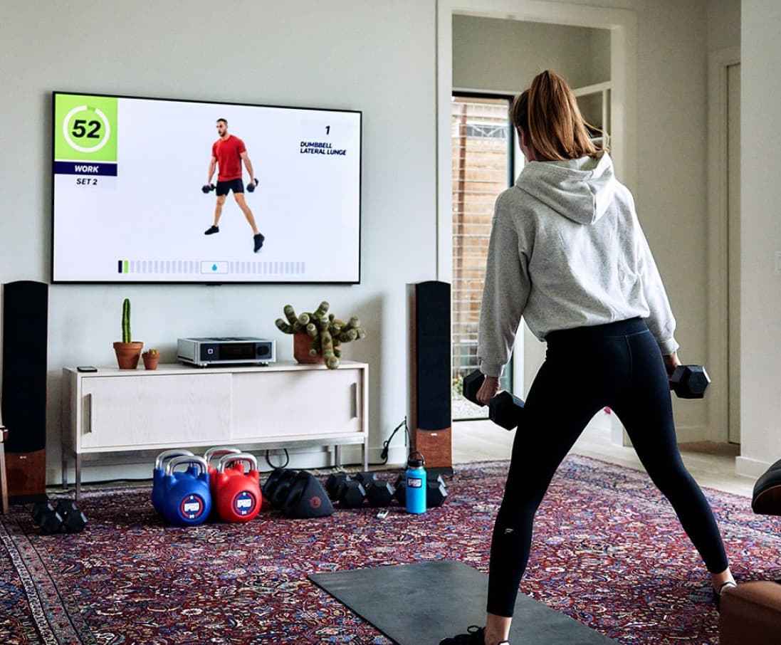 Woman at home carrying training weights working out in front of a TV following a F45 training program.