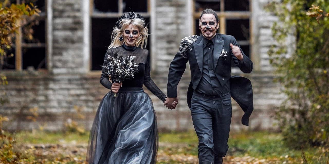 Fun Halloween photo of a young white couple running towards the camera wearing gray-black formalwear and gray and black face paint.