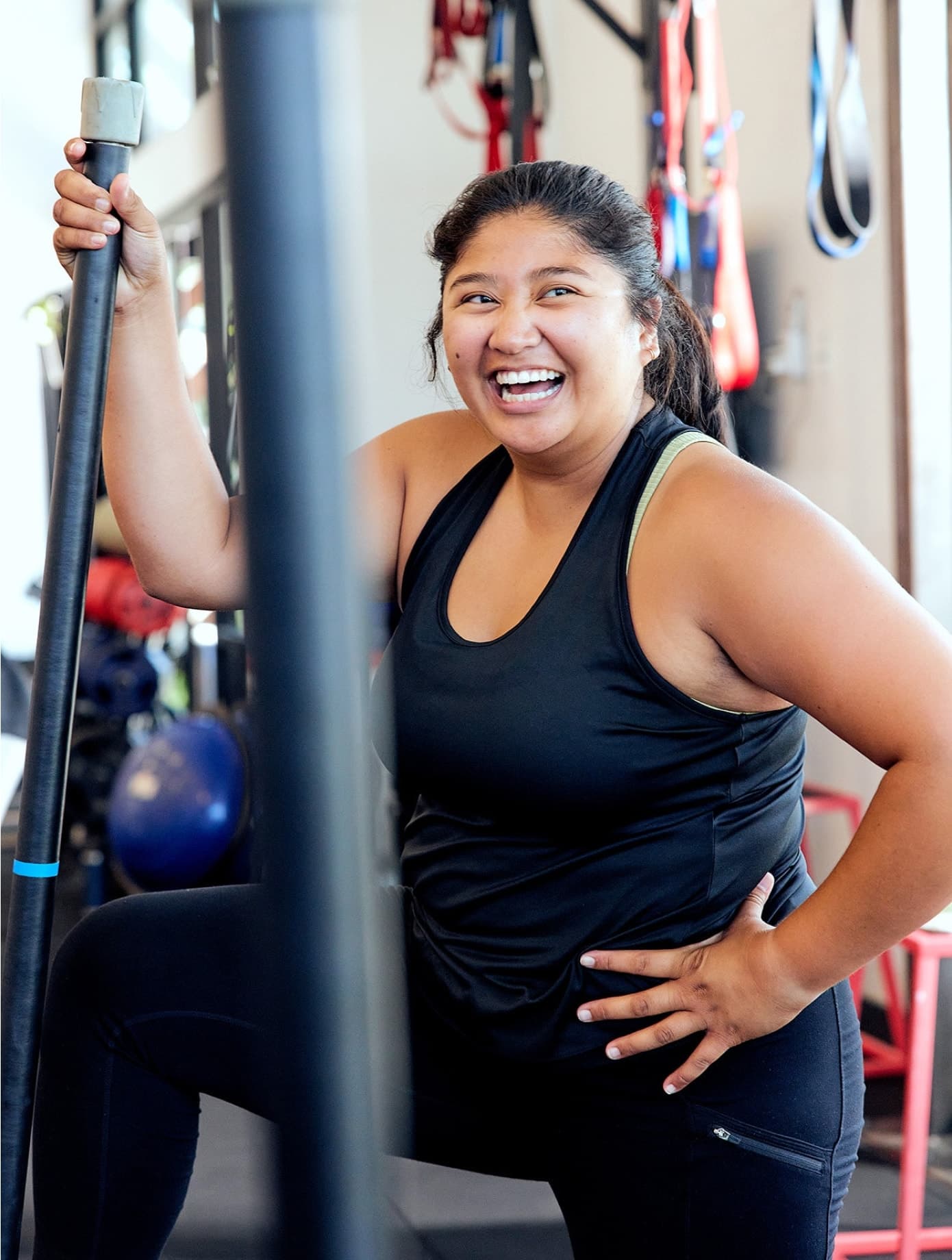 Smiling woman in black atheltic wear at F45 Training gym holding bar with one leg on bench