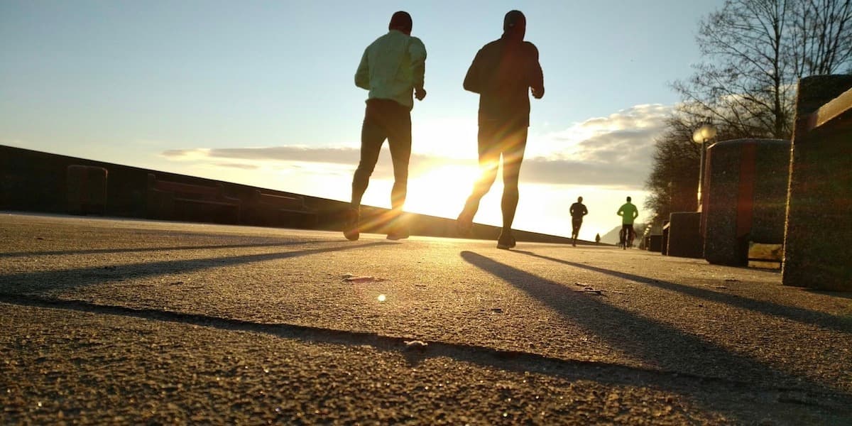 A view from the ground of four runners as seen from behind, dressed in full running gear, and running into the sunrise or sunset.