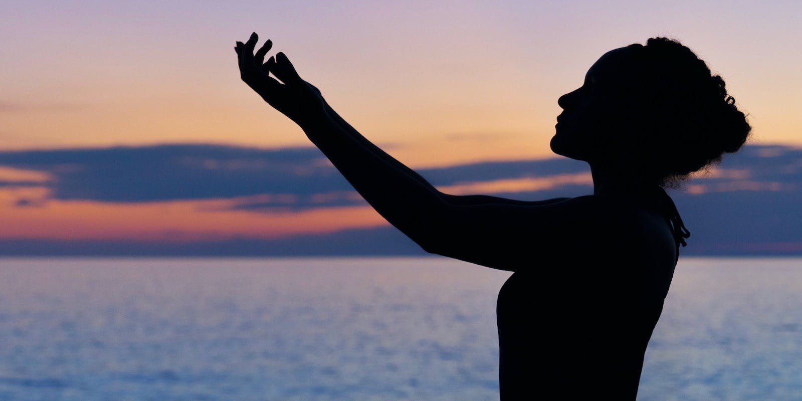The profiled silhouette of a woman with a sunset behind her. Her arms are stretched and raised in front of her.