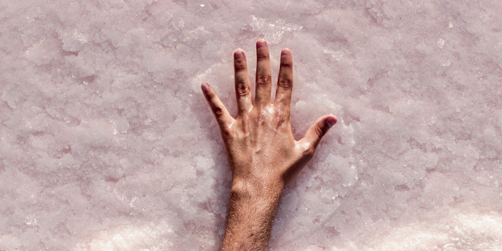 A glossy hand stretches out on a bed of wet pink salt.