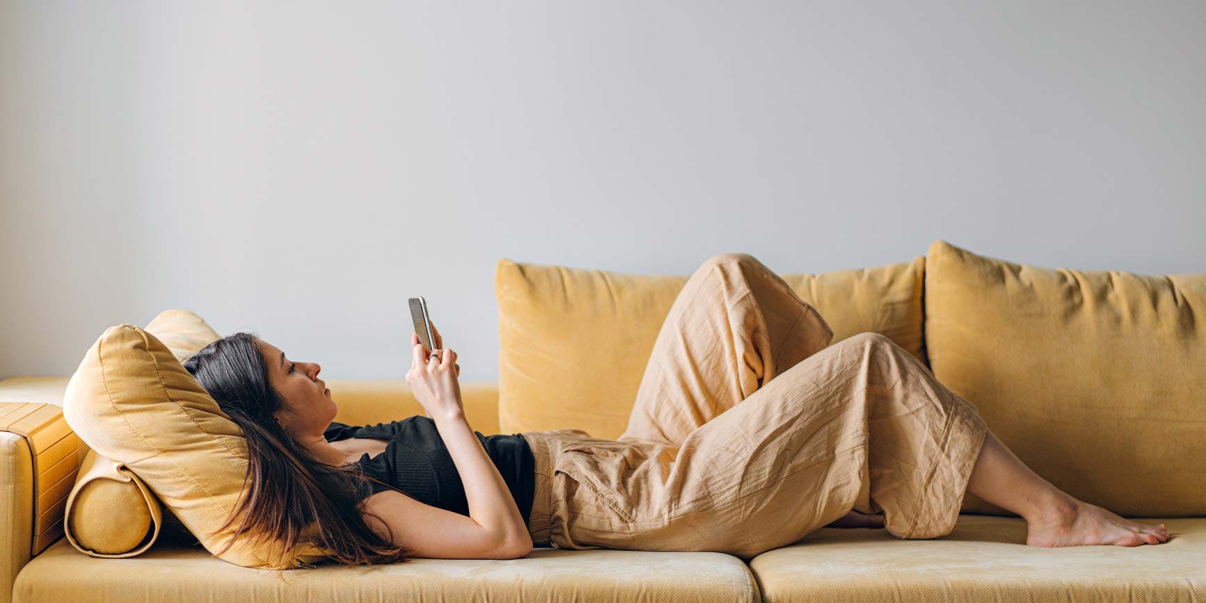 Woman lying down on yellow couch, interacting with her phone