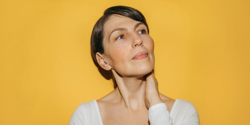 White, middle-aged woman looking to the right pensively against a marigold yellow background
