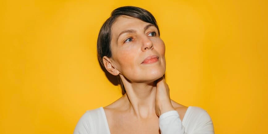 White, middle-aged woman looking to the right pensively against a marigold yellow background