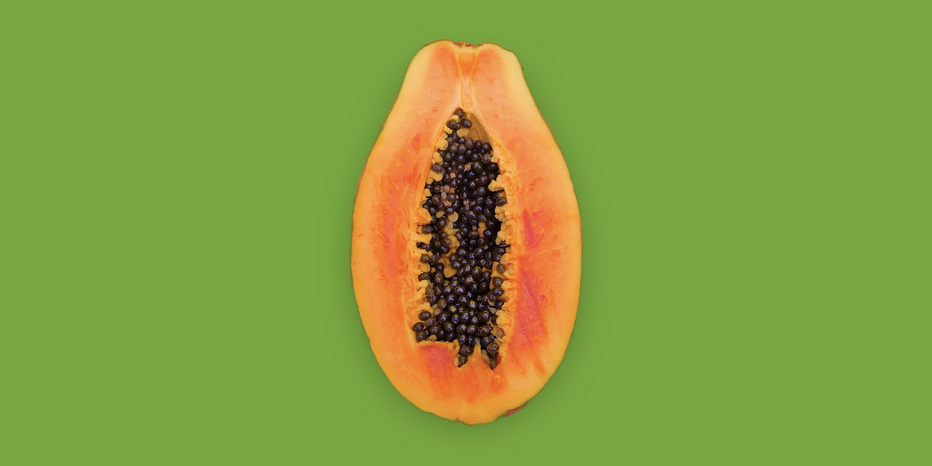 An orange papaya sliced in half sits against a grass green background