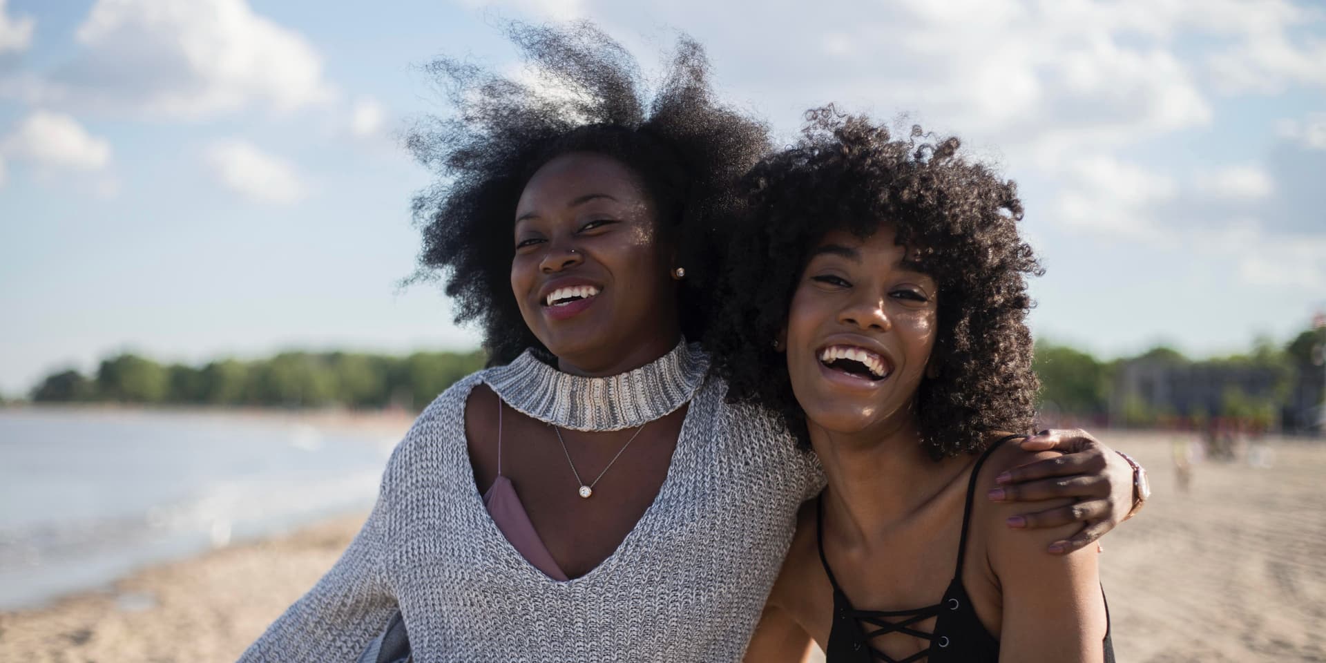 Two young black women with afros embracing and smiling at the beach on a sunny day