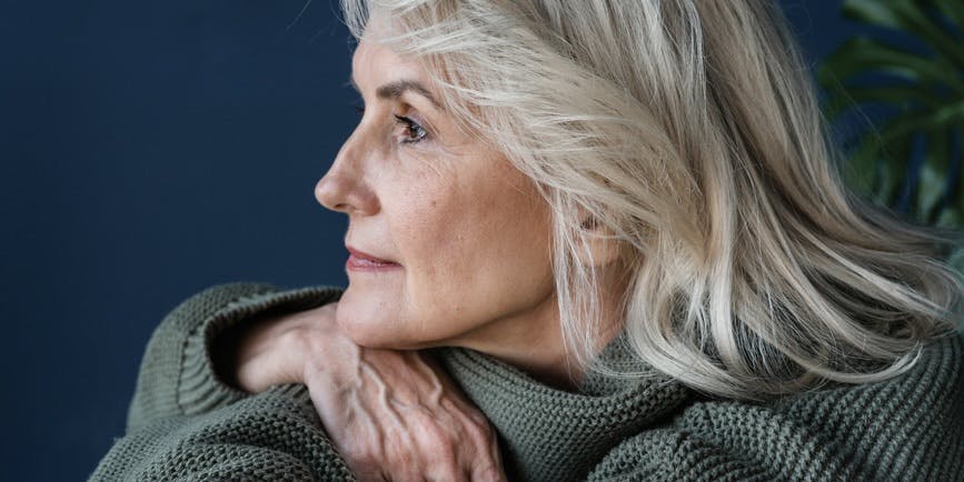 Una mujer blanca mayor está sentada con la cabeza en los brazos, mirando a lo lejos
