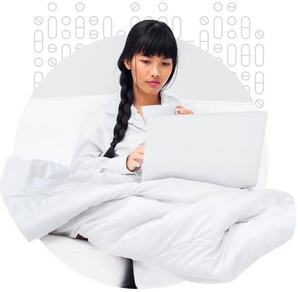 Mujer en pijama sentada en la cama, escribiendo en su portátil
