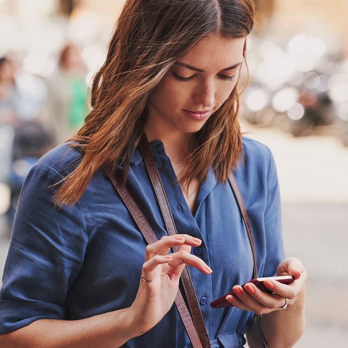 Mujer joven con blusa azul y un bolso, mirando su teléfono y a punto de tocarlo