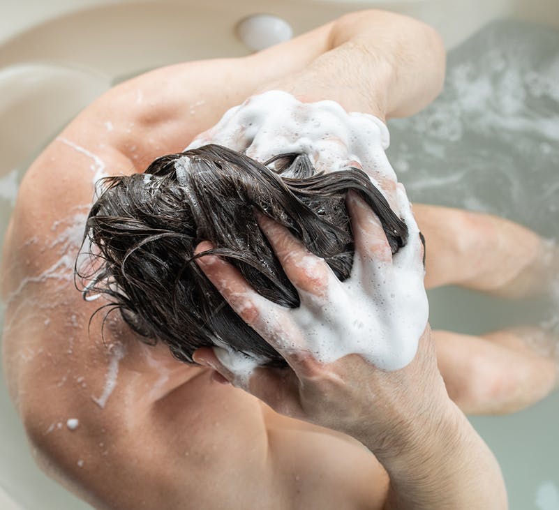 vista desde arriba, mirando hacia abajo, del hombre que se lava el pelo con ambas manos