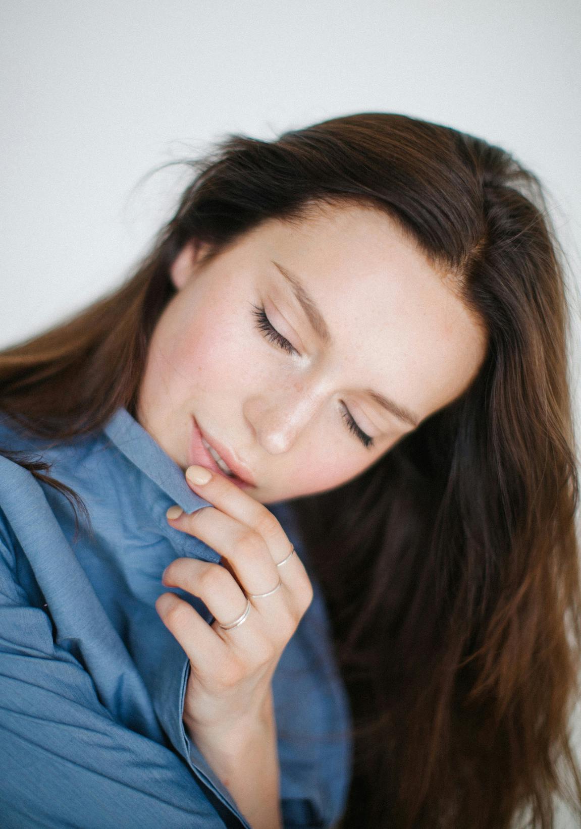 Woman touching her lips gently while tilting her head down to the right and closing her eyes