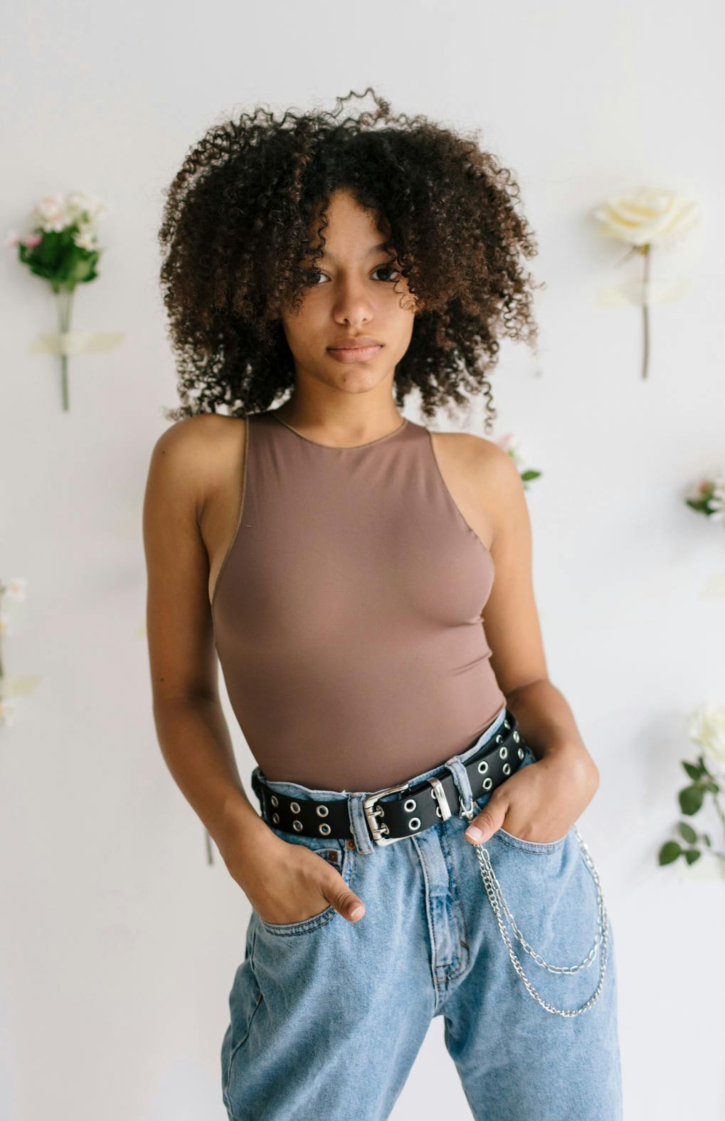 Young black woman with a head full of curly hair, confidently looking at camera, hips to the side, hands in pockets