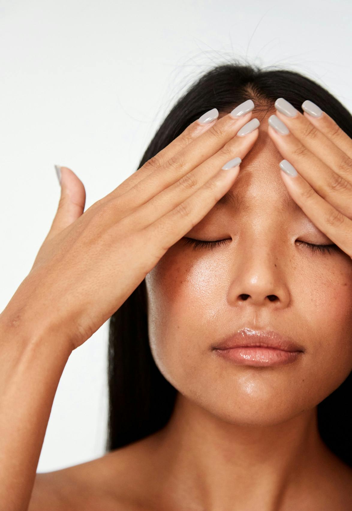 Close-up of Asian woman with her eyes closed. Both her hands are on her forehead.