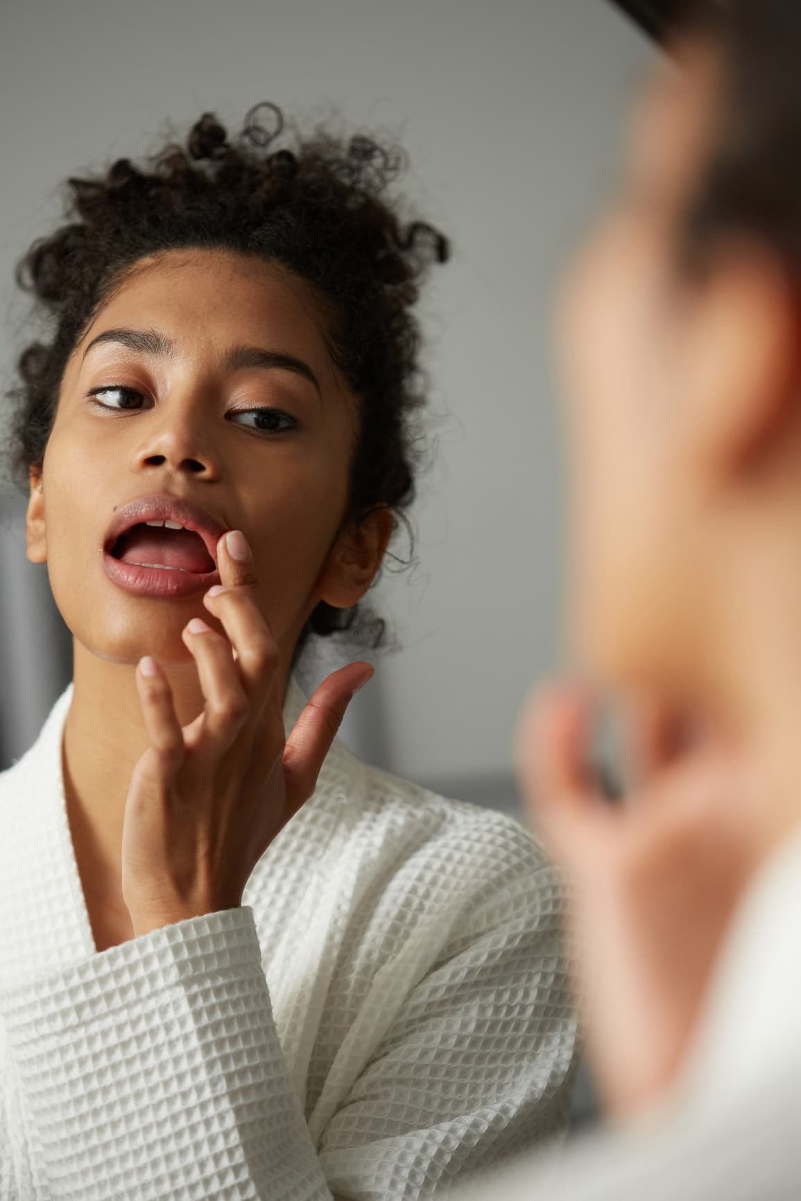 Mujer mirando de cerca su labio en el espejo, que está tocando con el dedo