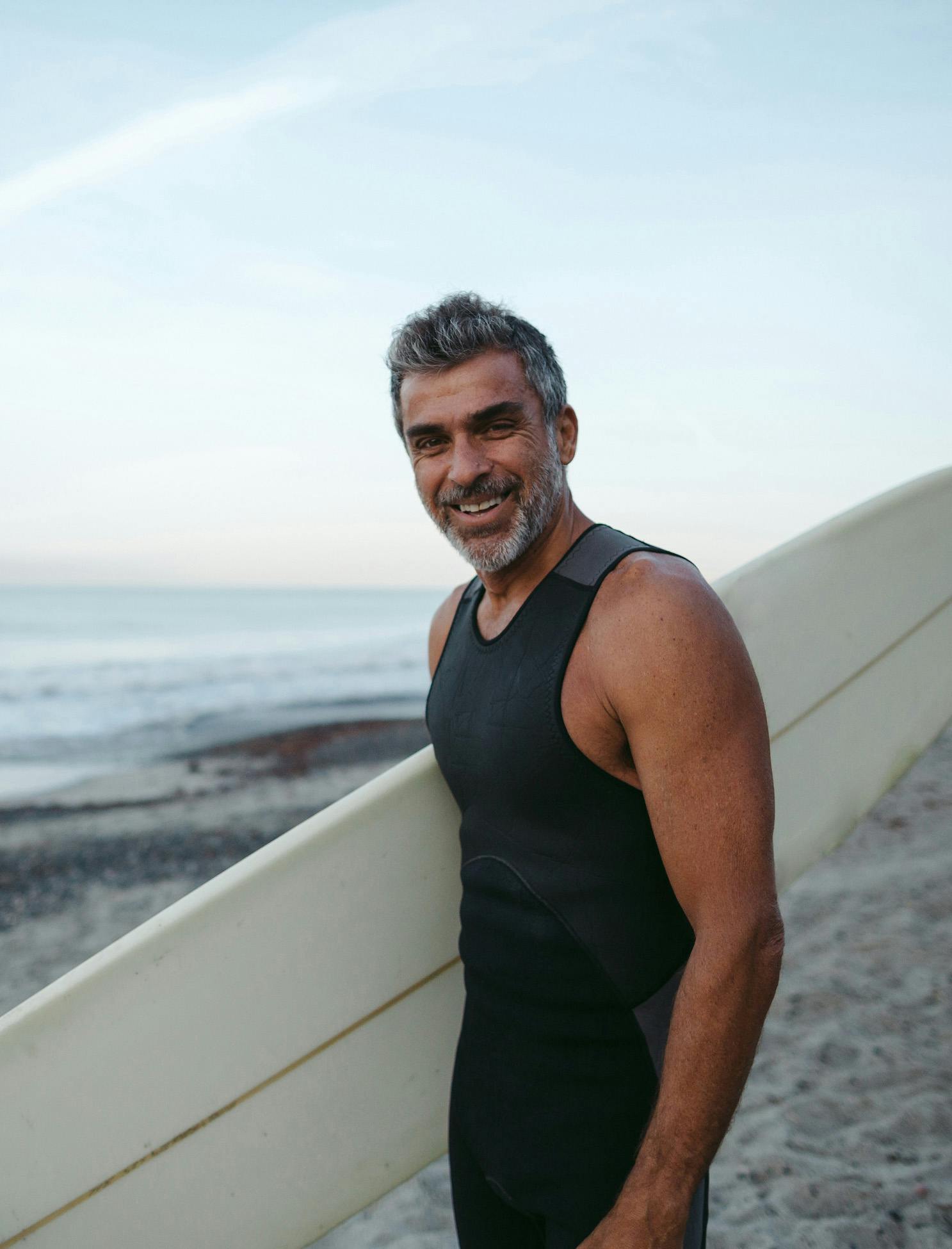 Man on beach smiling at camera, holding surfboard
