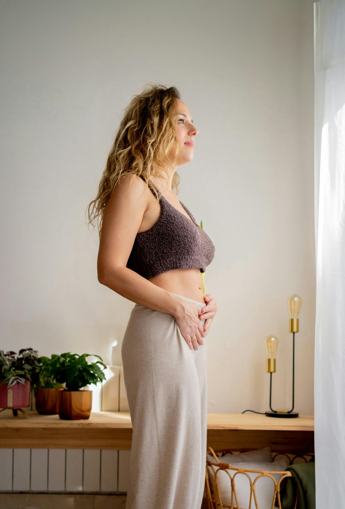 Woman looking out window while holding two hands on her stomach