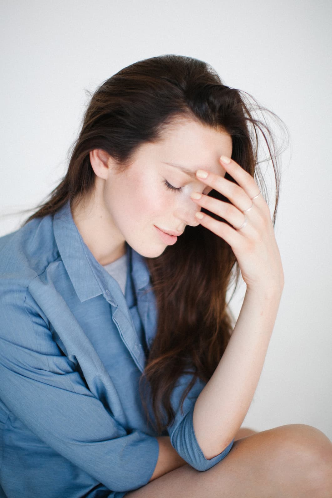 A woman, sitting cross-legged, elbows on leg, bowing her head with her eyes closed while she gently massages a headache